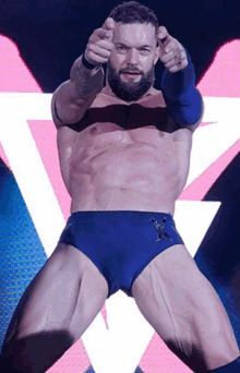 a man with a beard is pointing at the camera while wearing blue swim trunks