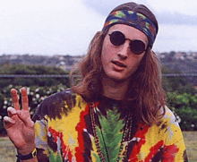 a man with long hair wearing sunglasses and a tie dye shirt