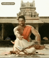 a man is sitting on a yoga mat in front of a temple with a book on a stand .