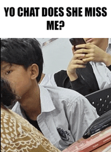 a boy is sitting in a classroom holding a cell phone and looking at it .