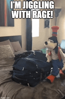 a stuffed goofy sitting on a bed next to a suitcase with the caption i 'm jigging with rage !