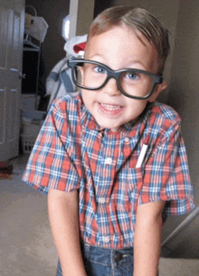 a little boy wearing glasses and a plaid shirt smiles for the camera