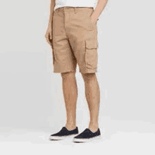 a man is wearing a pair of khaki cargo shorts and black sneakers .