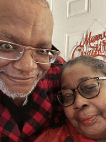 a man and a woman are posing for a picture with a merry christmas sign in the background