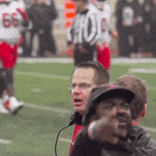 a man wearing glasses and a hat stands on a football field in front of a referee with the number 66 on his jersey