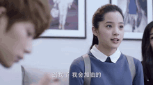 a woman in a blue sweater is talking to a man in a room with chinese writing on the wall .