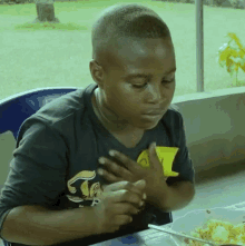 a young boy wearing a black shirt with the letter t on it is sitting at a table with a bowl of food ..