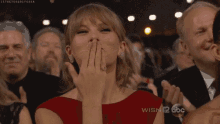 a woman in a red dress is covering her mouth with her hand while sitting in a crowd of people .