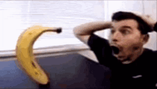 a man is looking at a banana with his mouth open and his hands on his head .