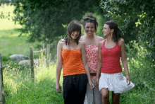 three young women are walking down a path in a field