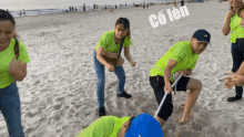 a group of people are playing tug of war on a beach and one of them is wearing a green shirt that says " co len "