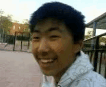 a young man is smiling and looking at the camera while standing in front of a fence .