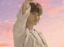 a young man is standing in front of a pink sky and raising his arm in the air .