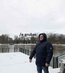 a man in a hooded jacket stands in front of a body of water with the words / e grubas written above him