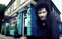 a man stands in front of a blue building with a sign that says ' the fox tavern ' on it