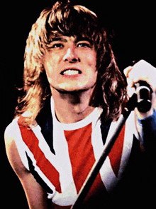 a man with long hair is singing into a microphone while wearing a red white and blue union jack shirt