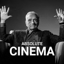 a black and white photo of a man sitting in a chair with his hands up .