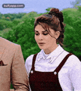 a woman in overalls is standing next to a man in a suit in a park .