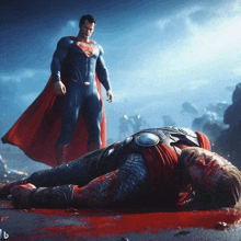 a man in a superman costume is standing next to a man in a thor costume laying on the ground