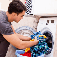 a man is putting clothes in a washing machine with a blue basket full of clothes