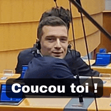 a man sitting in front of a microphone with the words coucou toi on the bottom