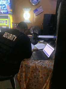 a man wearing a security vest is sitting at a table with a laptop