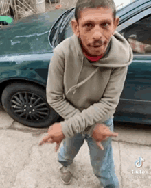 a man in a hoodie is standing in front of a green car .