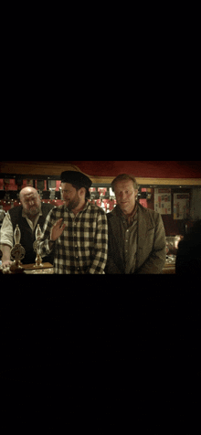 a man in a plaid shirt is talking to another man in a bar