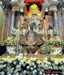 there is a statue of jesus in a glass dome on the altar surrounded by flowers .