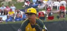 a young boy wearing a yellow hat with the letter w on it is playing baseball in front of a crowd .