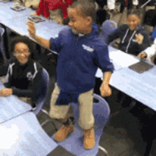 a young boy in a blue jacket is standing on a chair in front of a group of children .