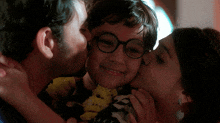 a young boy with glasses is kissed on the cheek by a man and woman