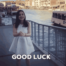 a woman in a white dress stands in front of a fence with the words good luck written below her