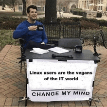 a man sits at a table with a sign that says linux users are the vegans of the it world