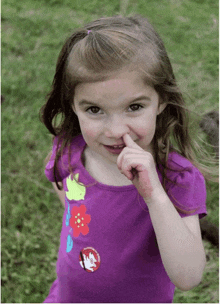 a little girl wearing a purple shirt with flowers on it holds her finger to her mouth