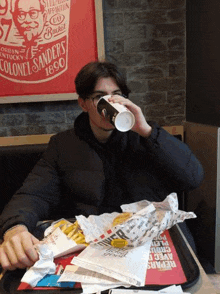 a man is drinking a cup of coffee while sitting at a table in a fast food restaurant .