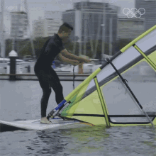 a man in a wet suit is standing on a surfboard in the water with the olympic rings in the background