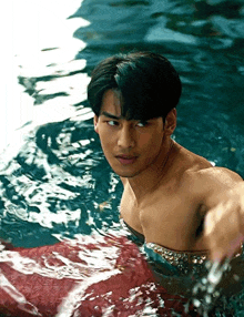 a shirtless man is swimming in a pool with a red skirt on