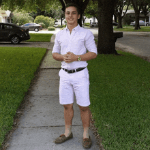 a young man in a white shirt and shorts stands on a sidewalk