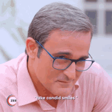 a man wearing glasses and a pink shirt with fake candid smiles written on the bottom