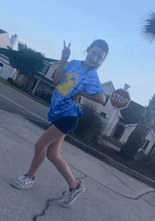 a girl in a blue tie dye shirt stands in front of a stop sign