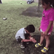 a little girl in a pink shirt is standing next to a little boy kneeling down in the grass .