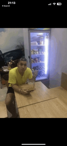 a man in a yellow shirt is sitting at a table in front of a refrigerator