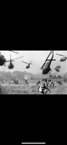 a black and white photo of a group of helicopters flying over a field .