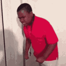 a man in a red shirt is crying while standing next to a door .