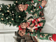 two boys and a baby wearing christmas pajamas are laying on a bed in front of a christmas tree