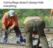 two men are working on train tracks and one of them is wearing camouflage .