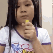 a young girl wearing a disney shirt is holding a yellow object in her hand .