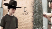 a young man wearing a cowboy hat is standing in front of a brick building with the word block on it .