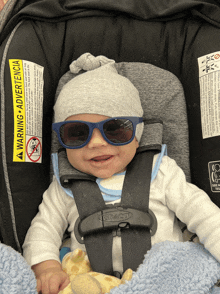 a baby wearing sunglasses is sitting in a car seat with a warning advertencia on it